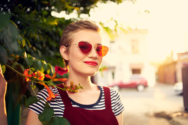 жінка в сонцезахисних окулярах на вулиці біля квітів, що позують стиль життя
 - Фото, зображення