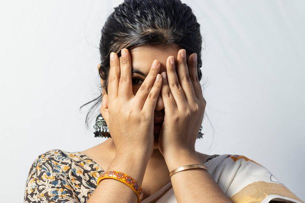 Elszigetelt fehér háttér egy indiai nő néz óvatosan az egyik szem arc borított kézzel fehér háttér - Fotó, kép
