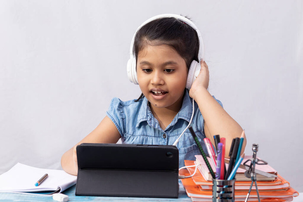 Hezká indická dívka dítě navštěvující online třídu s tabletem a sluchátkem na bílém pozadí - Fotografie, Obrázek