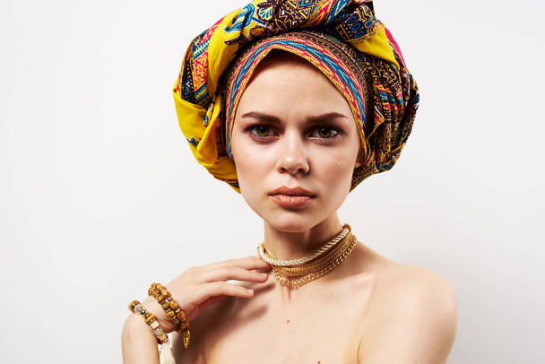 όμορφη γυναίκα κρατώντας το κεφάλι της διακόσμηση πολύχρωμο τουρμπάνι φως μόδας φόντο - Φωτογραφία, εικόνα