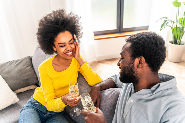 Black couple drinking sparkling wine at home to celebrate - Cheerful couple bonding and having aperitif - Foto, Imagen