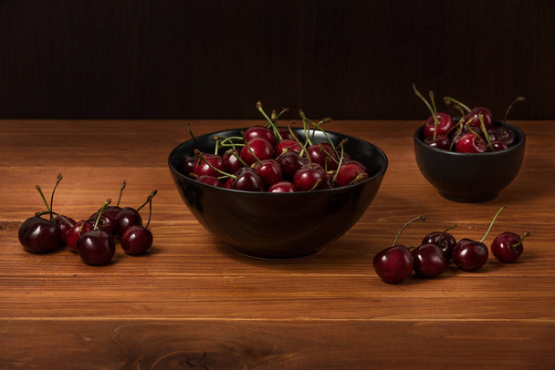 Ciotola piena di ciliegie rosse mature scure sulla superficie del tavolo di legno come fonte di vitamine, cibo biologico - Foto, immagini