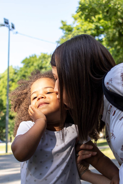 Mère caucasienne embrasse sa fille afro-américaine. Photo extérieure. - Photo, image
