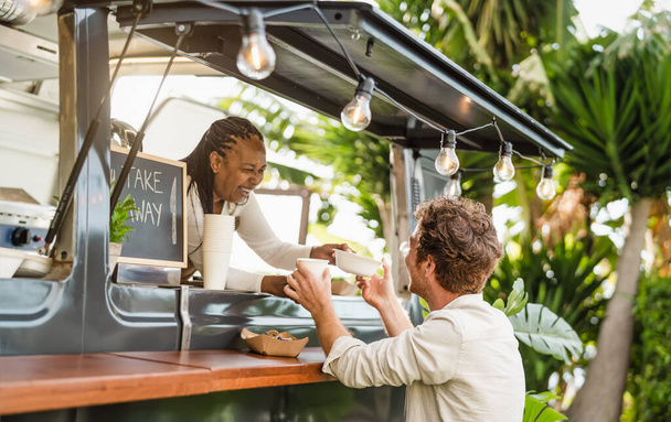 Afro food truck eigenaar serveren maaltijd aan mannelijke klant - Moderne business en take away concept - Foto, afbeelding