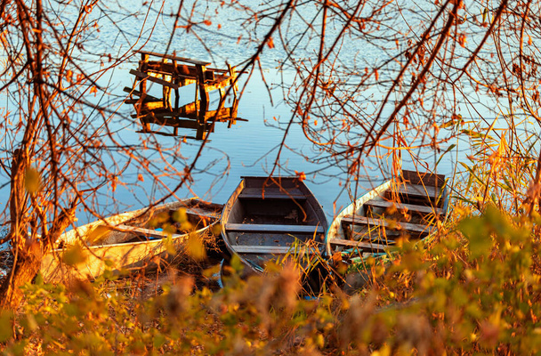 Herfstavond op een verlaten rivieroever met een oude visbrug en drie vissersboten. niemand - Foto, afbeelding