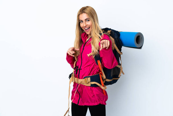 Молодая альпинистка с большим рюкзаком на изолированном белом фоне указывает пальцем на тебя - Фото, изображение
