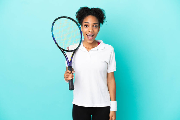 Genç tenisçi kadın mavi arka planda izole edilmiş ve yüzünde sürpriz bir ifade var. - Fotoğraf, Görsel