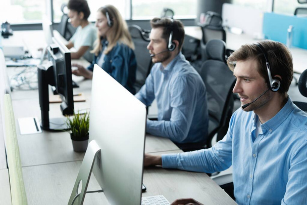 Young handsome male customer support phone operator with headset working in call center - Foto, afbeelding