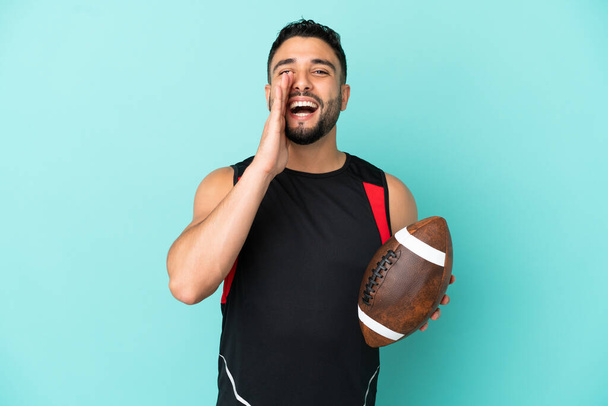 Young arab man playing rugby isolated on blue background shouting with mouth wide open - Photo, Image
