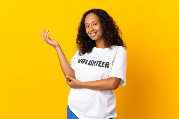 Teenager cuban volunteer girl isolated on yellow background extending hands to the side for inviting to come - Fotografie, Obrázek