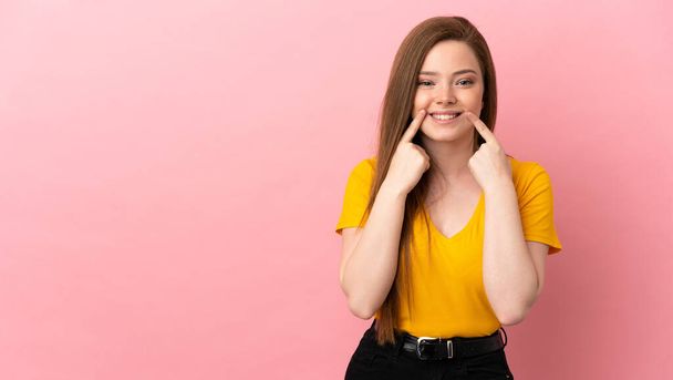 Девочка-подросток на изолированном розовом фоне улыбается со счастливым и приятным выражением лица - Фото, изображение