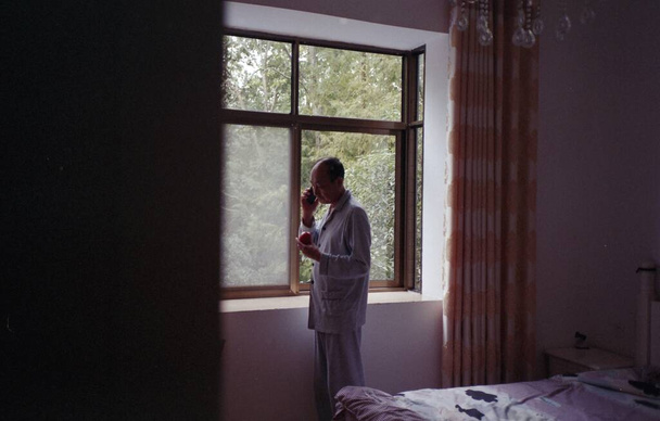 man in a white shirt and a black robe is looking at the window of a house - Foto, Imagem