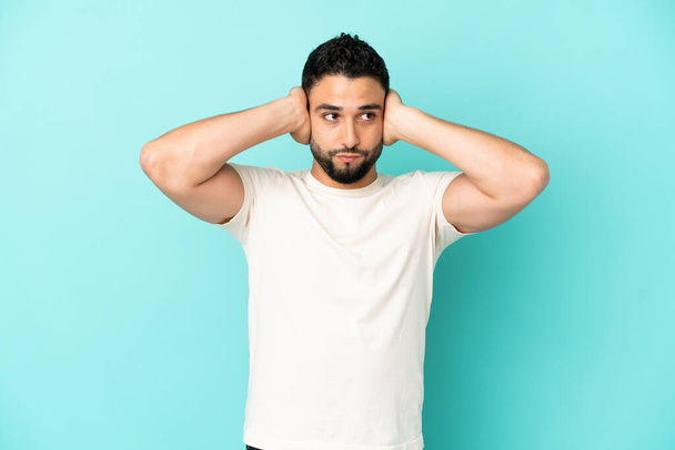 jovem árabe homem isolado no azul fundo frustrado e cobrindo orelhas - Foto, Imagem