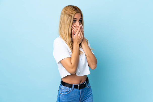 Jonge Uruguayaanse blonde vrouw over geïsoleerde blauwe achtergrond bedekken mond en kijken naar de zijkant - Foto, afbeelding