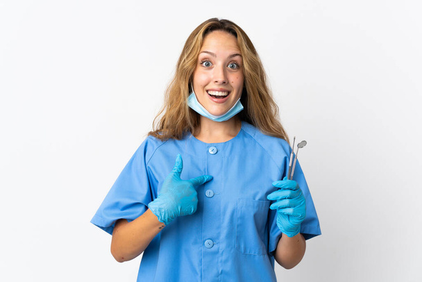 Nő fogorvos holding eszközök elszigetelt fehér háttér meglepetés arckifejezés - Fotó, kép