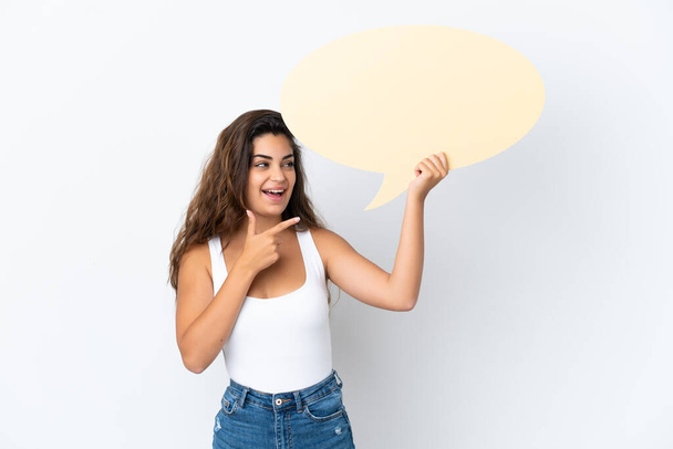 Young caucasian woman isolated on white background holding an empty speech bubble and pointing it - Foto, afbeelding