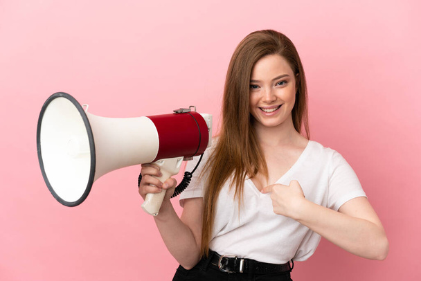 Teenager dívka přes izolované růžové pozadí drží megafon a s překvapením výraz obličeje - Fotografie, Obrázek