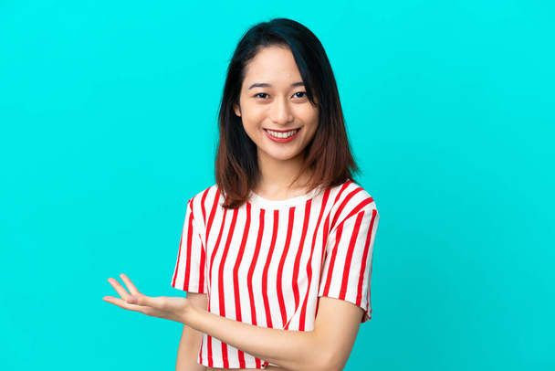 Jonge Vietnamese vrouw geïsoleerd op blauwe achtergrond presenteren van een idee terwijl het kijken glimlachen in de richting van - Foto, afbeelding