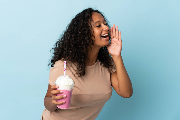 Teenager Mädchen mit Erdbeer Milchshake isoliert auf blauem Hintergrund schreit mit weit geöffnetem Mund zur Seite - Foto, Bild
