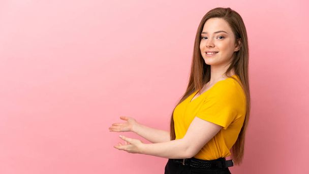 tiener meisje over geïsoleerde roze achtergrond uitbreiding van de handen naar de zijkant voor uitnodigen om te komen - Foto, afbeelding