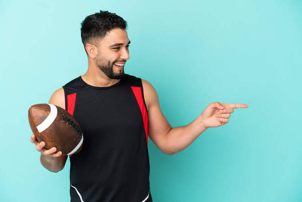Mladý arabský muž hraje rugby izolované na modrém pozadí ukazující prstem na stranu a prezentující produkt - Fotografie, Obrázek