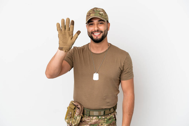 Junger arabischer Soldat auf weißem Hintergrund, der mit fröhlichem Gesichtsausdruck mit der Hand salutiert - Foto, Bild