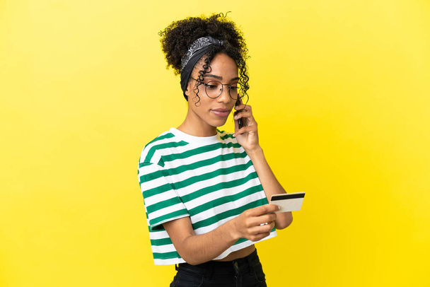 Fiatal afro-amerikai nő elszigetelt sárga háttér vásárol a mobil hitelkártyával - Fotó, kép