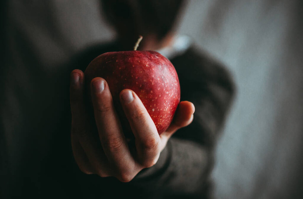 A closeup shot of a female hand holding a red apple isolated on blurred background - Fotoğraf, Görsel