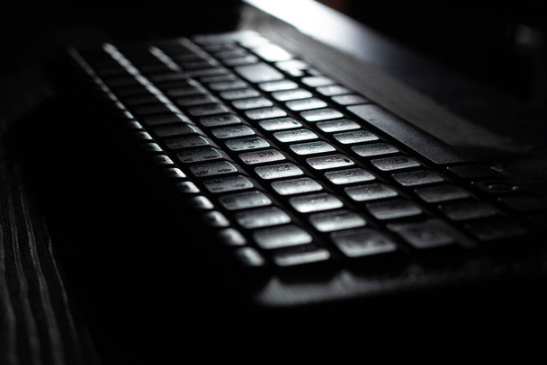 Комп'ютерна бездротова клавіатура з контрольною, функціональною та навігаційною алфавітно-цифровими клавішами та цифровою клавіатурою на дерев'яному фоні столу в офісі під час місячного світла. крупним планом
 - Фото, зображення
