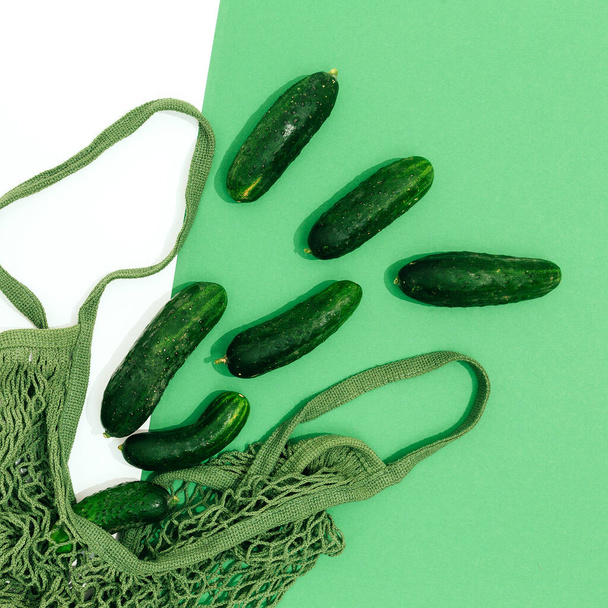 Minimalist fresh scene. Organic cucumber and mesh bag on green and white background. Zero waste, bio market, eco, vegan, raw concept.  Stylish flat lay - 写真・画像