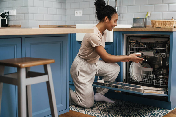 Happy black woman smiling while using dishwasher at home kitchen - Valokuva, kuva