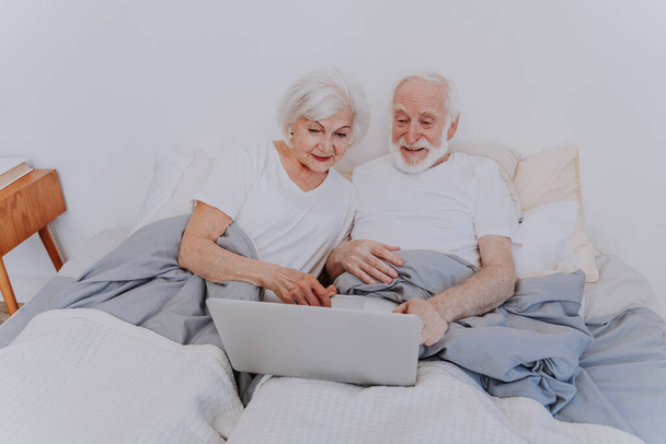 Beautiful senior couple enjoying time together at home - Moder elderly couple surfing the internet on laptop computer - Фото, изображение