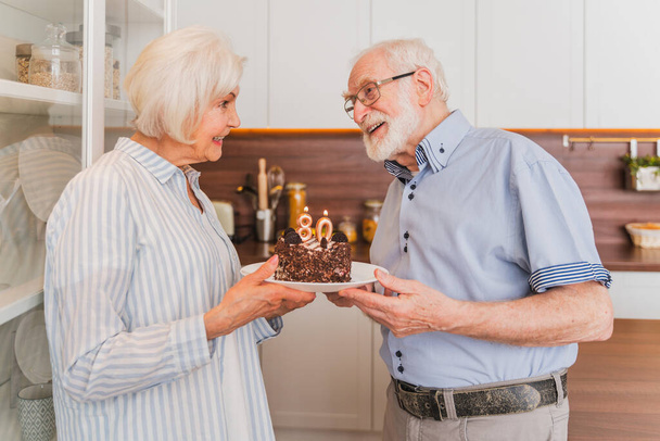 Beautiful senior couple celebrating  anniversary with birthday cake - Elderly couple having birthday party at home - Photo, Image