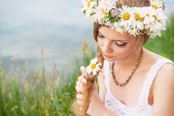 Cute young woman with circlet of camomile braiding her hair at t - Fotografie, Obrázek