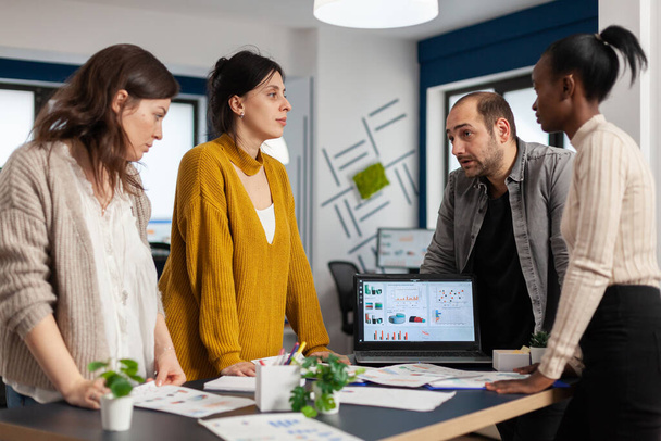 Различные деловые люди общаются в офисе стоя над столом - Фото, изображение