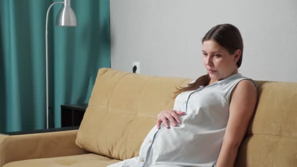 Беременная женщина, занимающаяся дыхательными упражнениями, испытывает схватки, сидя на диване - Кадры, видео