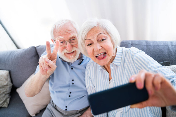 Happy senior couple having fun and taking photograph on mobile phone to share online on social networks - Elderly people using modern technology, grandparents taking selfie - Foto, Imagem