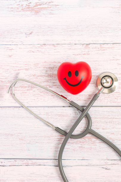 Rote Kugelherzform mit lächelndem Symbol und medizinischem Stethoskop mit Blick auf den oberen Tisch. Gesundheitswesen, Medicare und Kardiologie-Konzept. - Foto, Bild