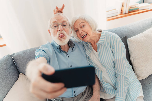 Happy senior couple having fun and taking photograph on mobile phone to share online on social networks - Elderly people using modern technology, grandparents taking selfie - Foto, Imagem