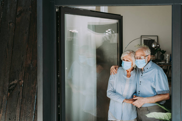 Elderly couple with protective face masks at home during covid-19 pandemic quarantine - Old people in quarantine respection social distance and isolation on coronavirus virus spread - Fotó, kép