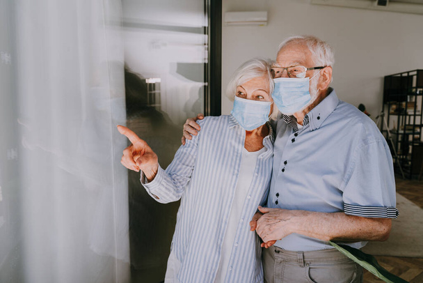 Elderly couple with protective face masks at home during covid-19 pandemic quarantine - Old people in quarantine respection social distance and isolation on coronavirus virus spread - Foto, imagen