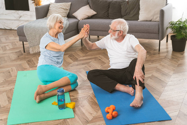 Sportive senior couple doing fitness and relaxation exercises at home - Elderly people training to stay healthy and fit - Foto, afbeelding