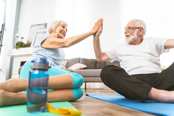 Sportive senior couple doing fitness and relaxation exercises at home - Elderly people training to stay healthy and fit - Fotó, kép