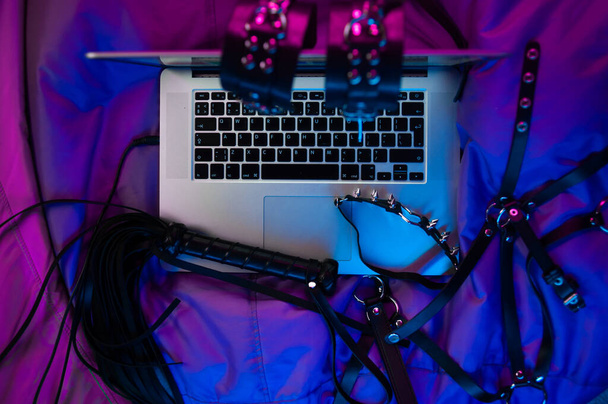 Een set van BDSM speelgoed voor seks op een laptop op een heldere neon achtergrond - Foto, afbeelding