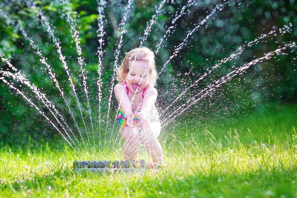 klein meisje spelen met tuin sprinkler - Foto, afbeelding