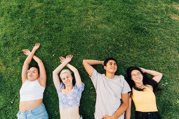 Grupa młodych wielonarodowych przyjaciół na świeżym powietrzu leżąca trawa uśmiechnięta i relaksująca - reklama copyspace - Zdjęcie, obraz