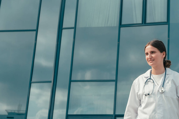 confident young female doctor standing near a large hospital building . - Fotó, kép