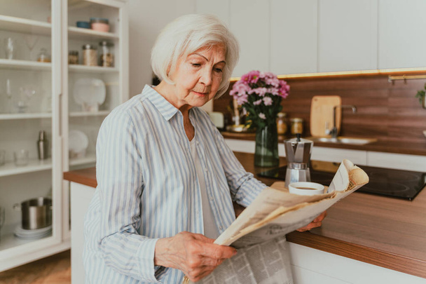 Senior woman relaxing at home, reading newspaper and having breakfast - Фото, изображение