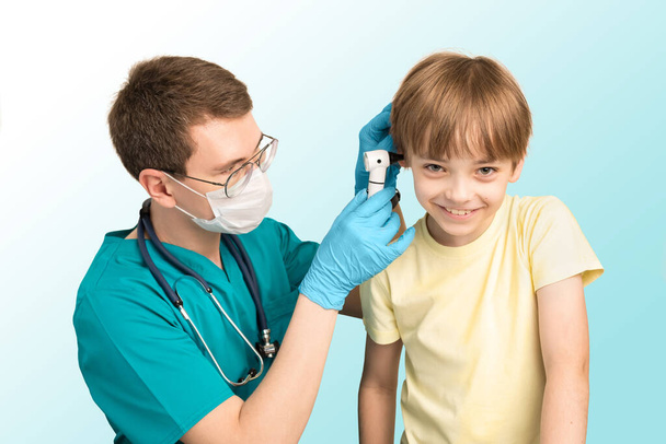 Pediatric pediatrician man examines the ears of the child with an otoscope in the clinic. The boy smiles. White background - Фото, изображение