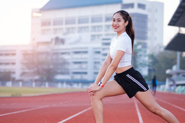 A young beautiful Asian woman in sports outfits doing stretching before workout outdoor in the park in the morning to get a healthy lifestyle. Healthy young woman warming up outdoors - Photo, Image